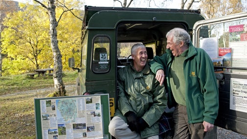 Two men in the welcome team smile from the National Trust truck in Great Wood car park on a sunny autumn day
